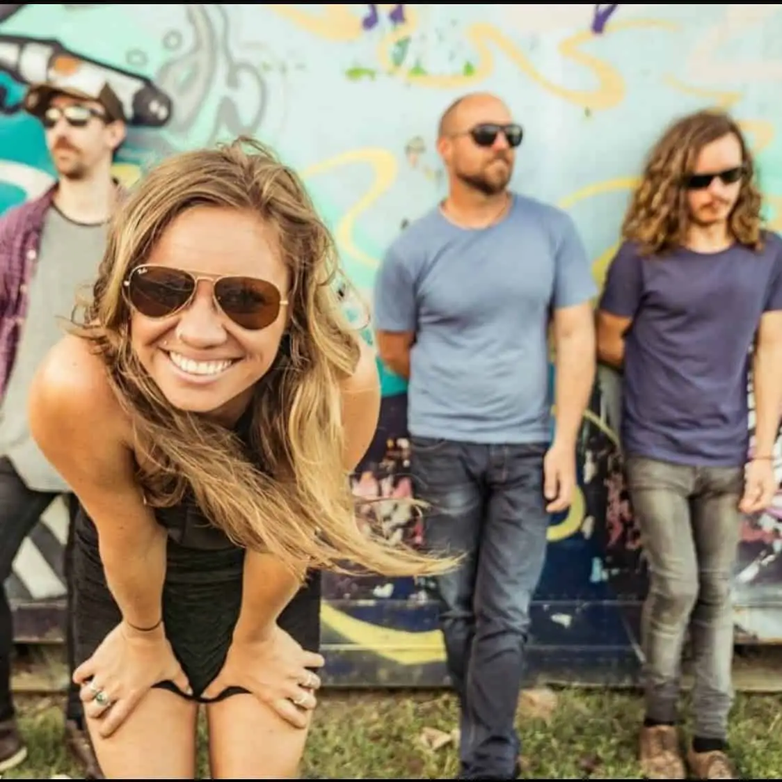 Photo of band, young lady smiling in foreground while 3 men stand in background